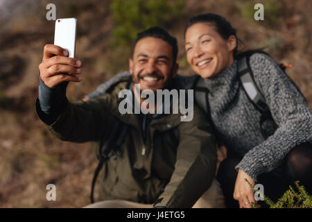 Young couple hiking taking selfie with smart phone. Happy young man and woman taking self portrait. Stock Photo