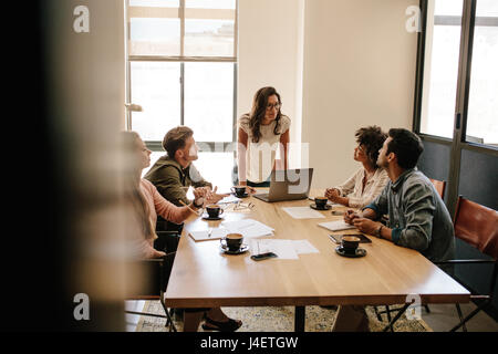 Shot of multi ethnic business people having a meeting in office. Business team sitting around a table with woman giving presentation.
