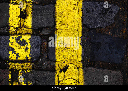 Double yellow lines with cracked paint on a cobbled London street. vertical composition, rule of thirds. Stock Photo