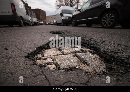 A large pot hole revealing underlying bricks on a road in Bristol. Stock Photo