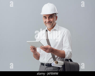 Construction engineer connecting with a digital tablet and using apps, he is wearing a safety helmet Stock Photo
