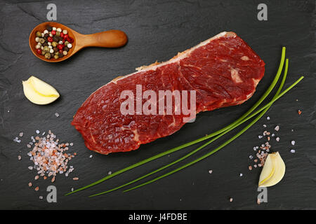 Raw beefsteak red meat cut, spices, peppercorns, spring shallot onions, garlic and salt on black slate board, close up, elevated top view, directly ab Stock Photo