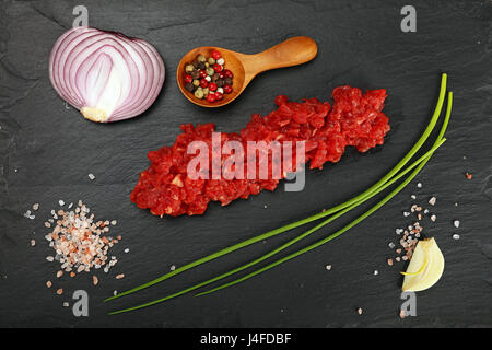 Raw minced beef red meat cutlet, spices, peppercorns, spring shallot onions, garlic and salt on black slate board, close up, elevated top view, direct Stock Photo