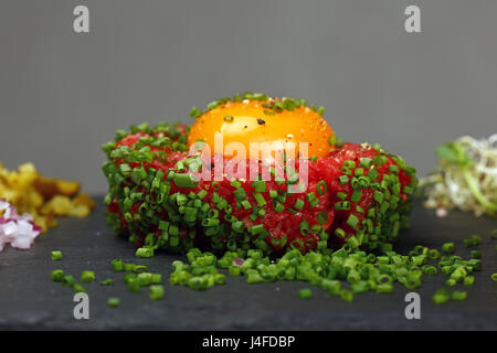 One portion of raw minced beef meat tartare steak with egg yolk ant green shallot onions served on black slate board, close up, low angle side view Stock Photo