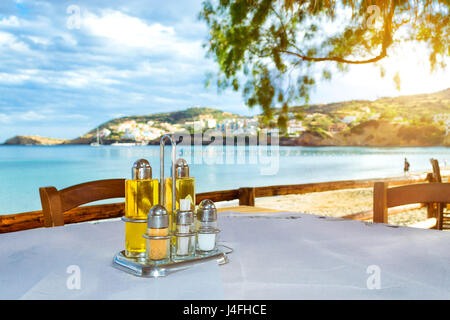 Cooking set olive oil, salt, pepper, condiments and toothpicks are on table at beach cafe on the seafront. Livadi beach in sea bay of resort village B Stock Photo