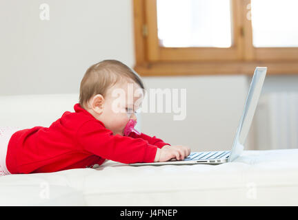 Eight months old baby girl using a laptop on the couch at home. Stock Photo