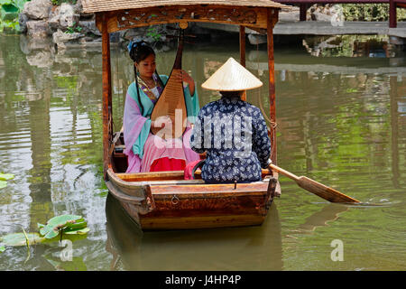 Two ladies sit in a small boat, one is playing a Pipa while one is paddling,  on a large pond in the Garden of the Humble Administrator.i Suzhou Stock Photo