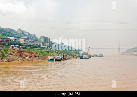 Ships moored close to a large manufacturing facility on the banks of the Yangtze River, near the town of Fuling, on a hazy morning Stock Photo