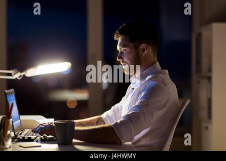 man with laptop and coffee working at night office Stock Photo