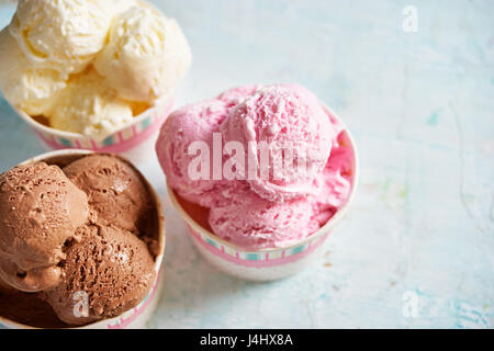 Three sorts of ice cream in paper cups on shabby blue wooden table. Stock Photo