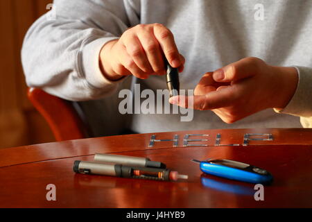 Diabetes. Blood glucose meter. Adult man measuring sugar level in blood at the table. Stock Photo