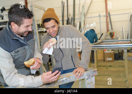 cheerful factory workers having lunch eating sandwich in a workshop Stock Photo