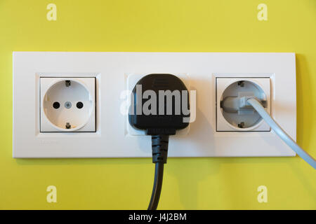 A british three-pin plug with a travel adapter plugged in next to a european two-pin plug Stock Photo