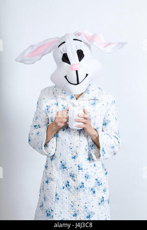 Rabbit difficult to wake in the morning Warming himself with an hot cup of coffee dressing-up clothes and conceptual parody Stock Photo