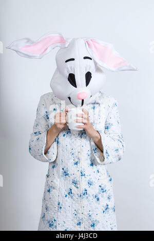 Rabbit difficult to wake in the morning. Warming himself with an hot cup of coffee. dressing-up clothes and conceptual parody Stock Photo