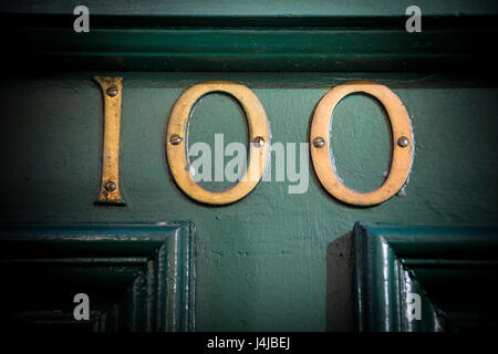 Number one hundred brass door number on weathered painted doorway Stock Photo