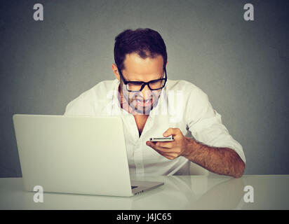 Angry stressed man having problems on line with a laptop talking texting on mobile phone with support service sitting at table Stock Photo