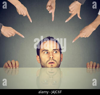 Scared man young employee hiding under the table being accused by many people who point fingers at him Stock Photo