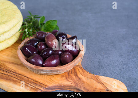 Mediterranean appetizer antipasti tapas calamara olives and garlic pita bread, herbs on wooden plank made from olive tree and grey background Stock Photo