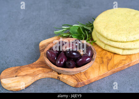 Mediterranean appetizer antipasti tapas calamara olives and garlic pita bread, herbs on wooden plank made from olive tree and grey background Stock Photo