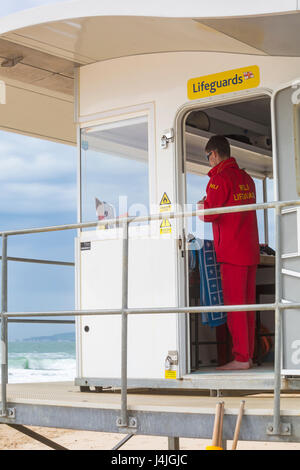 RNLI Lifeguard on duty patrolling the area in RNLI kiosk hut station at the seaside on Bournemouth beach in April Stock Photo