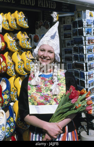 The Netherlands, Amsterdam, souvenir sales, woman, national costume, tulips, smile, half portrait Holland, Dutchwoman, locals, tradition, folklore, folklore clothes, flowers, tulip bunch, cut flowers, agriculture, botany, happily, friendly, contently, satisfaction, sales, souvenirs, postcards, clogs, memory, economy, Oranier route Stock Photo