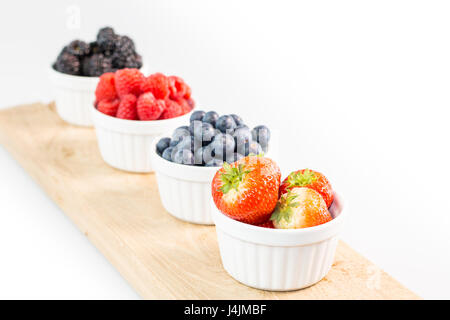 Strawberries, blueberries, raspberries and blackberries on wooden cutting board with shallow depth of field Stock Photo