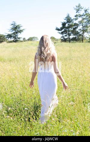 Young woman in long white dress walking in meadow. Stock Photo