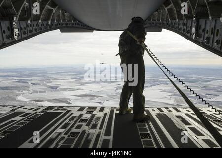 Staff Sgt. Brock Wranik, 62nd Operations Support Squadron loadmaster, looks on as a formation of six C-17 Globmaster IIIs prepare an airdrop over Rainier Drop Zone near Moses Lake, Wash., during the Rainier War exercise Dec. 7, 2016. The airdrop fulfilled one of the objectives of the exercise, which was to resupply members of the Army’s 7th Infantry Division with equipment and supplies. Stock Photo