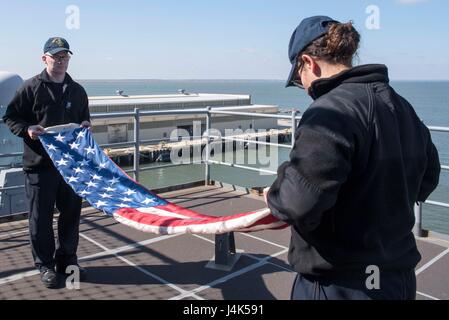 170320-N-WH681-052 ATLANTIC OCEAN (March 20, 2017) Hospital Corpsman 2nd Class Bradley Proctor (left) and Hospitalman Tyler Radcliff fold the ensign on the fantail of the amphibious assault ship USS Kearsarge (LHD 3). Kearsarge is currently underway conducting routine shipboard certifications. (U.S. Navy photo by Mass Communication Specialist Seaman Kaitlyn E. Eads/Released) Stock Photo