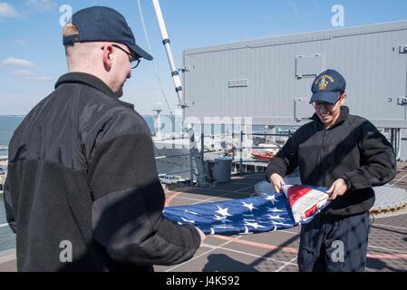 170320-N-WH681-055  ATLANTIC OCEAN (March 20, 2017) Hospital Corpsman 2nd Class Bradley Proctor, left, and Hospitalman Tyler Radcliff fold the ensign on the fantail of the amphibious assault ship USS Kearsarge (LHD 3). Kearsarge is underway conducting routine shipboard certifications. (U.S. Navy photo by Mass Communication Specialist Seaman Kaitlyn E. Eads/Released) Stock Photo