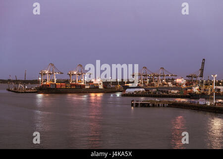 Auckland, New Zealand - March 6, 2017: Overview of the container terminal at sunset with ships. Lights on the docks reflected in the water. Stock Photo