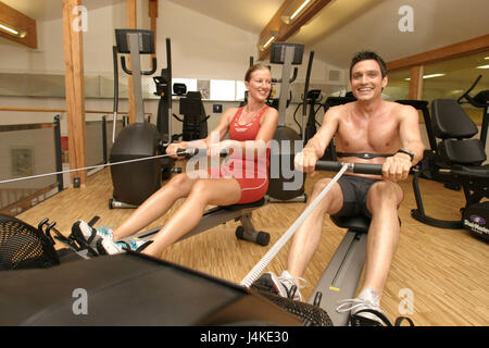 Fitness studio, couple, young, smile, do not coach oar devices freely for fitness studio sport, sportily, health, training, warming up, warm-up, perseverance, stamina training, perseverance sport, ergometer, oar ergometer, row, drag, motion, muscle construction, capacity, increase in output, hobby, leisure time, conscious of health, conscious of body, conscious of character, together Stock Photo