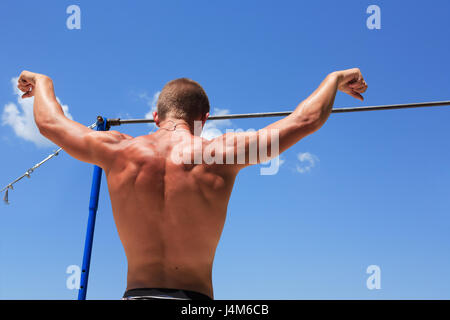 Young strong athlete standing before horizontal bar against blue sky Stock Photo
