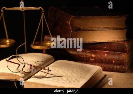 Vintage still life with spectacles on open book near brass weight scale on dark background Stock Photo