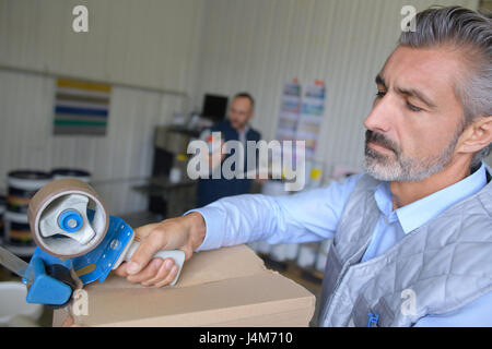 Man using tape dispenser to seal cardboard box Stock Photo
