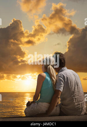 Caucasian couple admiring scenic view of sunset at ocean Stock Photo
