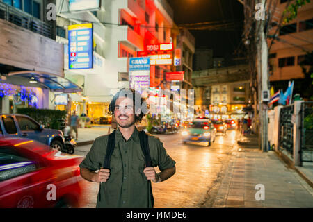 Smiling man carrying backpack in city at night Stock Photo