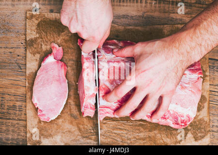 Hands of man cutting raw meat on butcher paper with knife Stock Photo