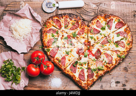 Heart-shaped pizza and ingredients on cutting board Stock Photo