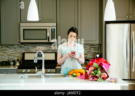 Woman texting on cell phone in domestic kitchen Stock Photo