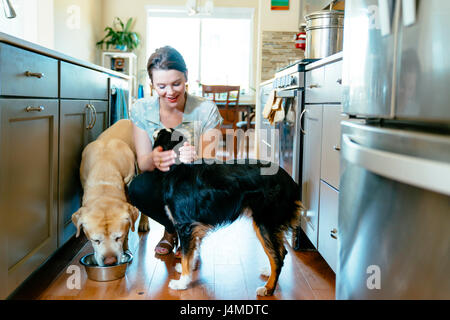 Woman feeding and petting dogs in domestic kitchen Stock Photo