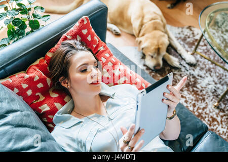 Woman laying on sofa near dog using digital tablet Stock Photo