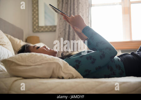 Mixed Race woman laying on bed using digital tablet Stock Photo