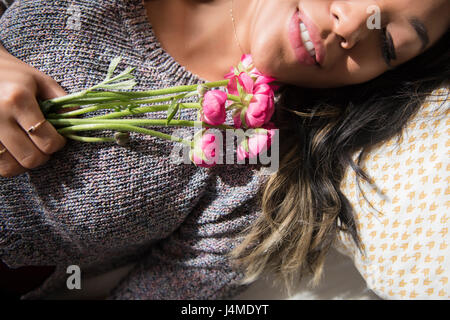 Mixed Race woman laying on bed holding flowers Stock Photo