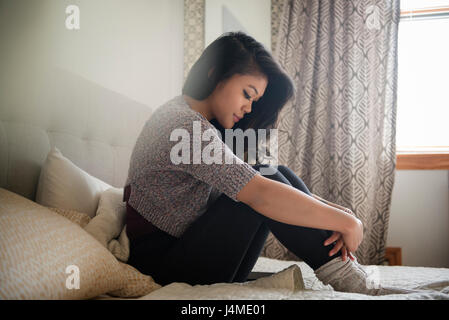 Depressed Mixed Race woman sitting on bed Stock Photo
