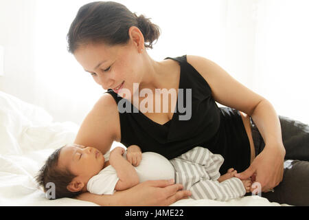 Mother laying on bed cradling sleeping baby son Stock Photo