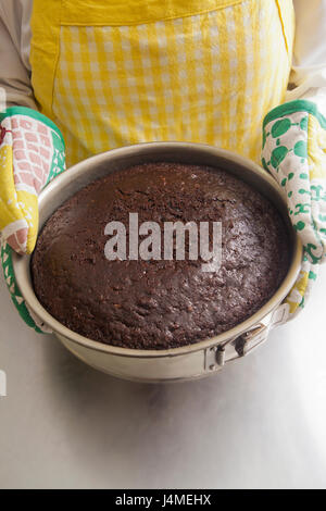 Hispanic woman holding cake in pan with oven mitts Stock Photo