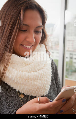 Smiling Hispanic woman texting on cell phone Stock Photo