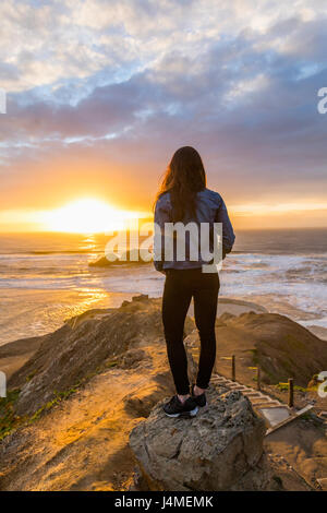 Caucasian woman standing on rock near ocean at sunset Stock Photo